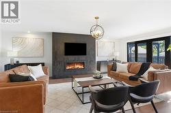 Spacious living area featuring a modern fireplace insert within a dark textured accent wall, recessed lighting, a contemporary brass chandelier, and dark-framed double doors opening to an exterior are -