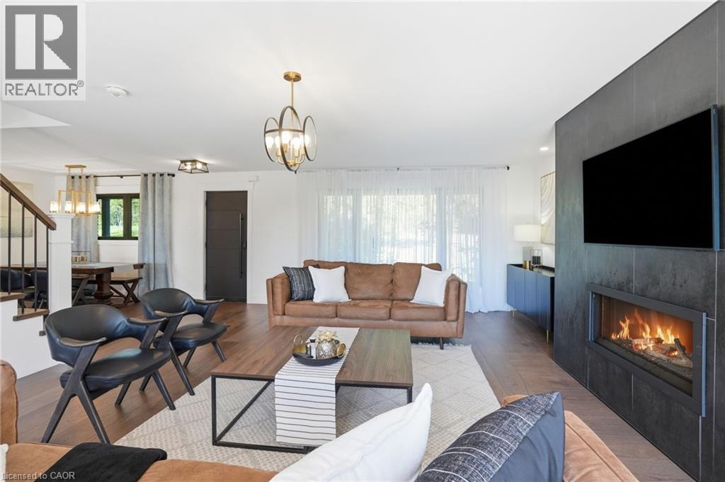 Spacious living area featuring wood-finish flooring, a contemporary fireplace with dark-toned tile surround, and an open layout - 71 Miles Road, Hamilton, ON