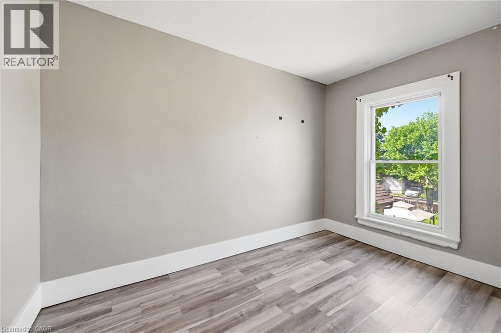 Room featuring a single window with view into backyard, light gray walls, white baseboards, and wood-finish flooring - 343 Cumberland Avenue, Hamilton, ON