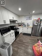 Modern kitchen featuring white shaker cabinetry with black hardware, stainless steel appliances, and wood-finish flooring -