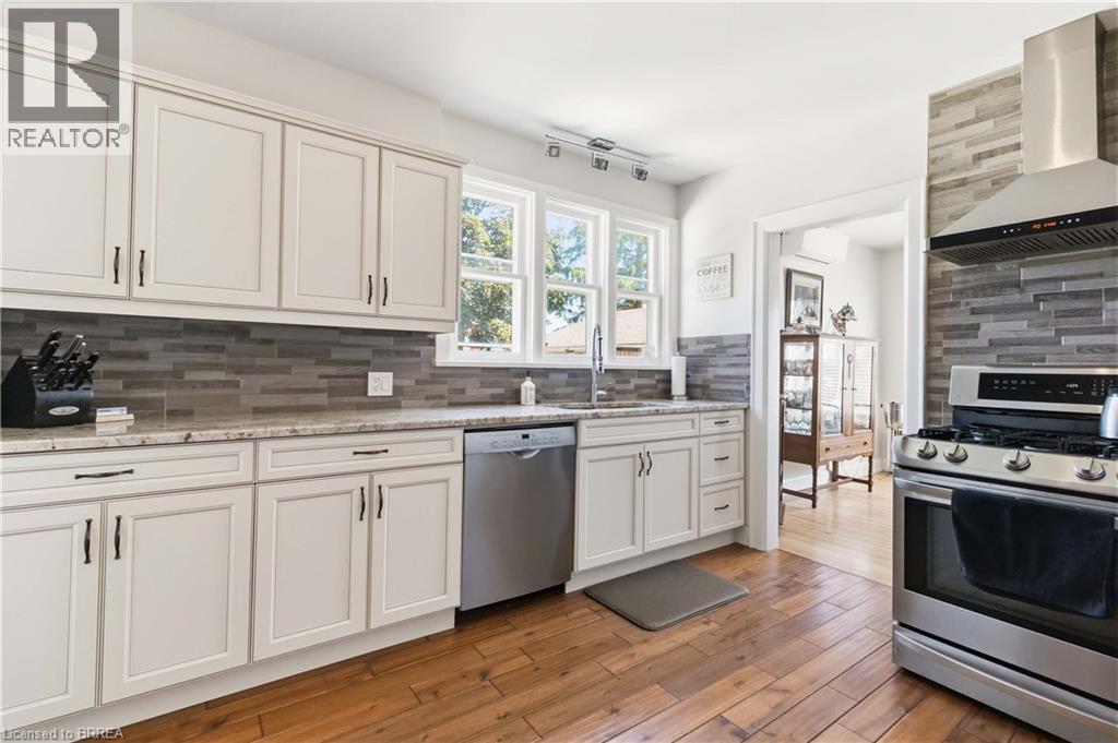 Kitchen featuring white cabinetry, granite countertops, a horizontal stacked tile backsplash, stainless steel appliances, and wood-finish flooring - 134 Queensway Drive, Brantford, ON