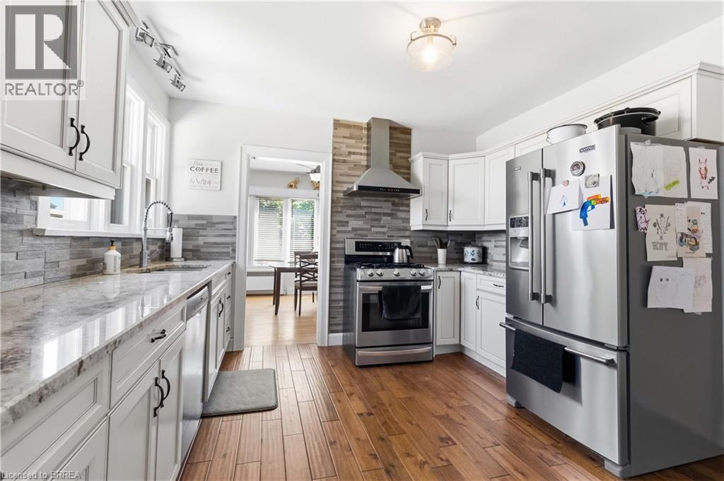 Kitchen featuring shaker-style white cabinetry, stainless steel appliances, a stacked stone backsplash, wood-finish flooring, and light-toned countertops - 134 Queensway Drive, Brantford, ON