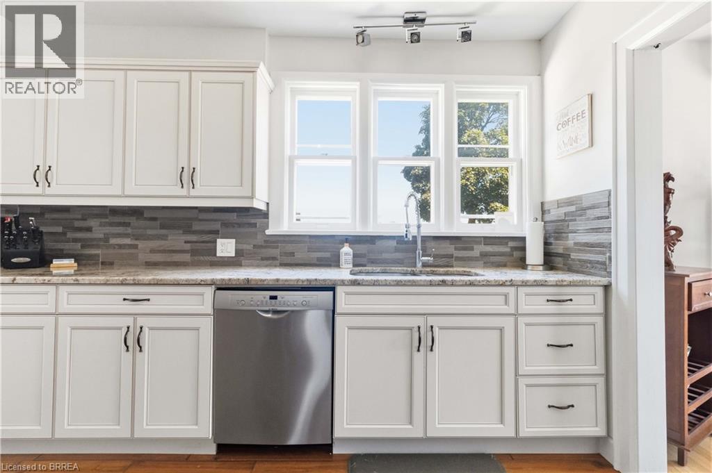 Kitchen featuring white shaker cabinetry, stone countertops, a tiled backsplash, stainless steel dishwasher, and a window above the sink - 134 Queensway Drive, Brantford, ON
