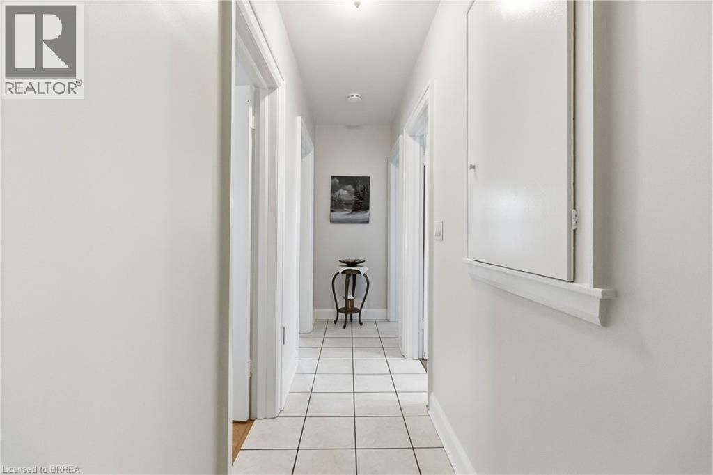 Hallway featuring square tile flooring, multiple doorways, and a wall-mounted panel with trim - 134 Queensway Drive, Brantford, ON