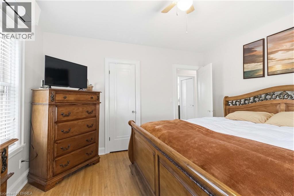 Hardwood flooring extends throughout this interior space, featuring a ceiling fan, white paneled doors, and a window with white blinds - 134 Queensway Drive, Brantford, ON