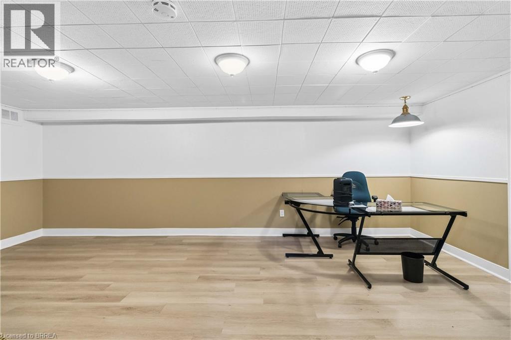 Spacious room featuring wood-finish flooring, drop ceiling with recessed lighting, two-tone painted walls, and baseboard trim - 134 Queensway Drive, Brantford, ON