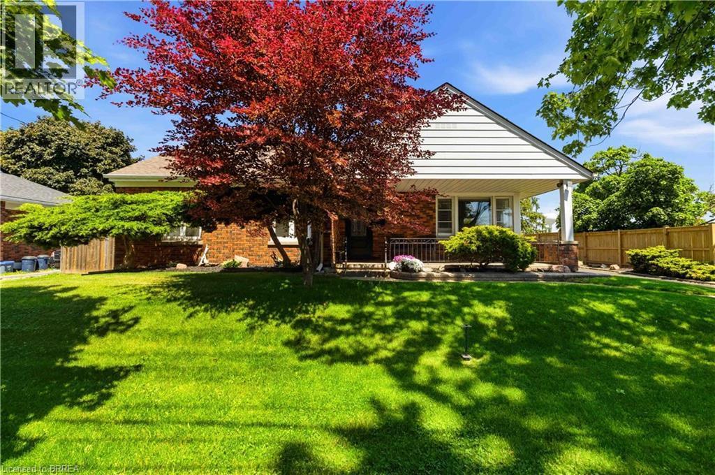 Front exterior featuring a covered porch with stone-clad columns, white siding, and a brick facade - 134 Queensway Drive, Brantford, ON