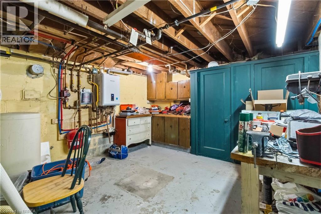 Basement utility featuring a tankless water heater, exposed overhead plumbing, wood-finish cabinetry, and a concrete floor - 134 Queensway Drive, Brantford, ON