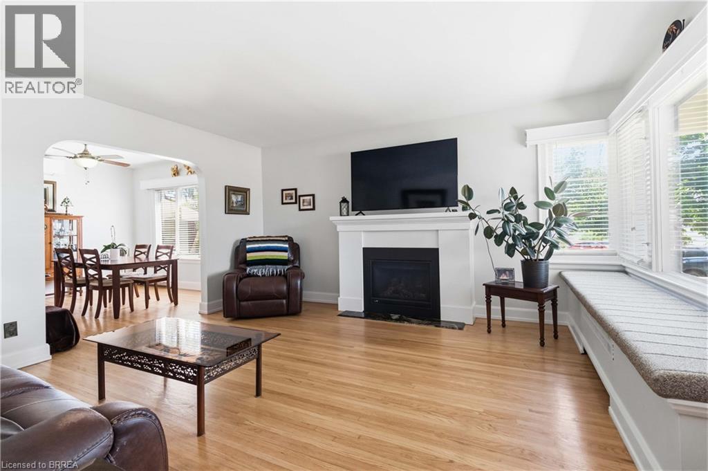 Bright living area featuring wood-finish flooring, a white mantel fireplace, multiple windows with blinds, and an integrated window seat - 134 Queensway Drive, Brantford, ON