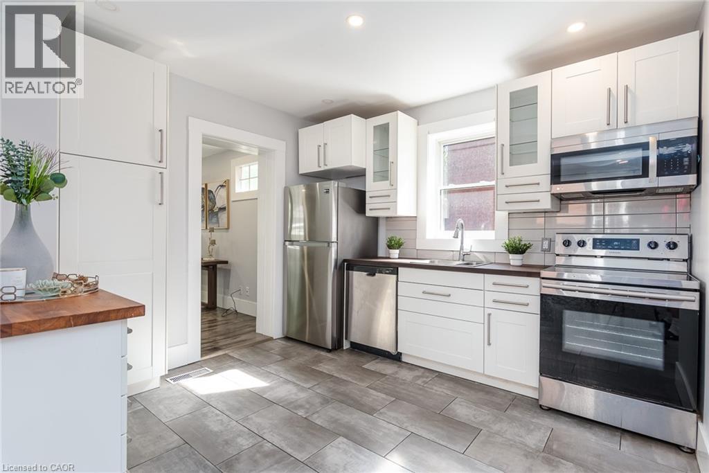 Kitchen featuring wood-finish flooring, white cabinetry, stainless steel appliances, a built-in microwave, and a window above the sink - 40 Woodland Avenue, Kitchener, ON