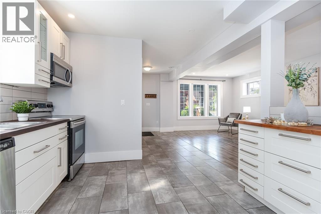 Contemporary kitchen featuring white cabinetry, stainless steel appliances, dark countertops, and a white subway tile backsplash - 40 Woodland Avenue, Kitchener, ON
