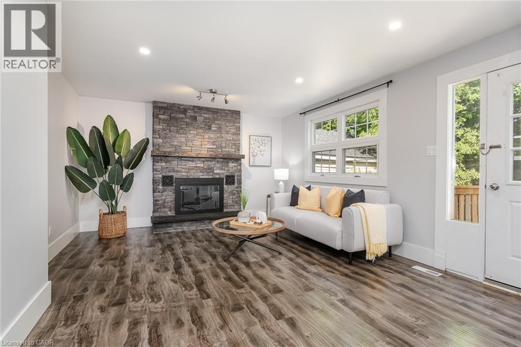 Living area featuring wood-finish flooring, a stone-clad fireplace with a dark mantel, recessed lighting, and a white framed window - 40 Woodland Avenue, Kitchener, ON