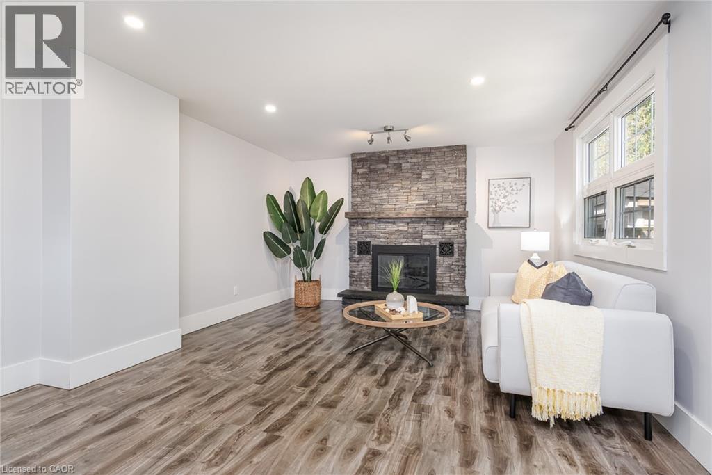 Living area featuring a stone-clad fireplace with a wood mantel, wood-finish flooring, recessed lighting, and a double-pane window - 40 Woodland Avenue, Kitchener, ON