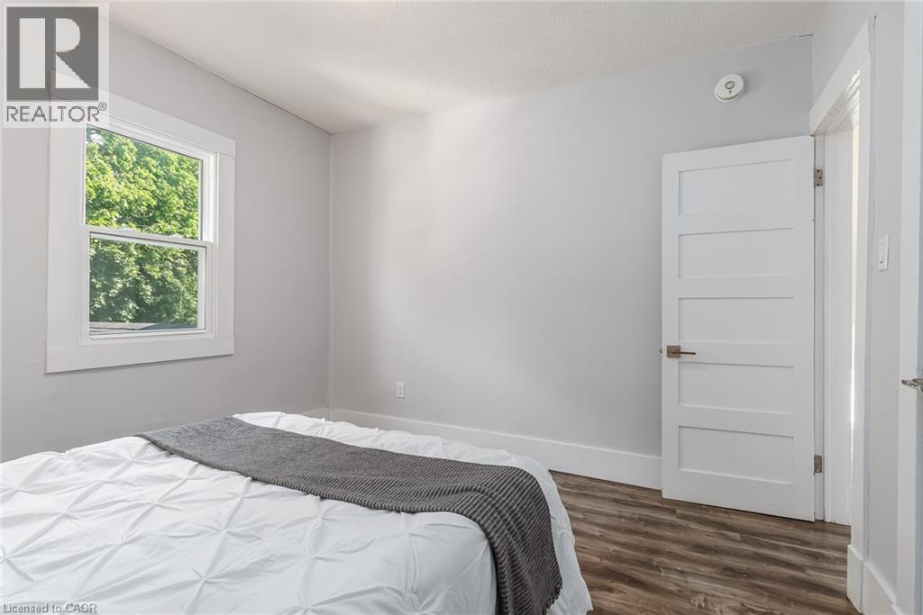Bedroom featuring light gray walls, white trim, a large window, a five-panel interior door, and wood-finish flooring - 40 Woodland Avenue, Kitchener, ON