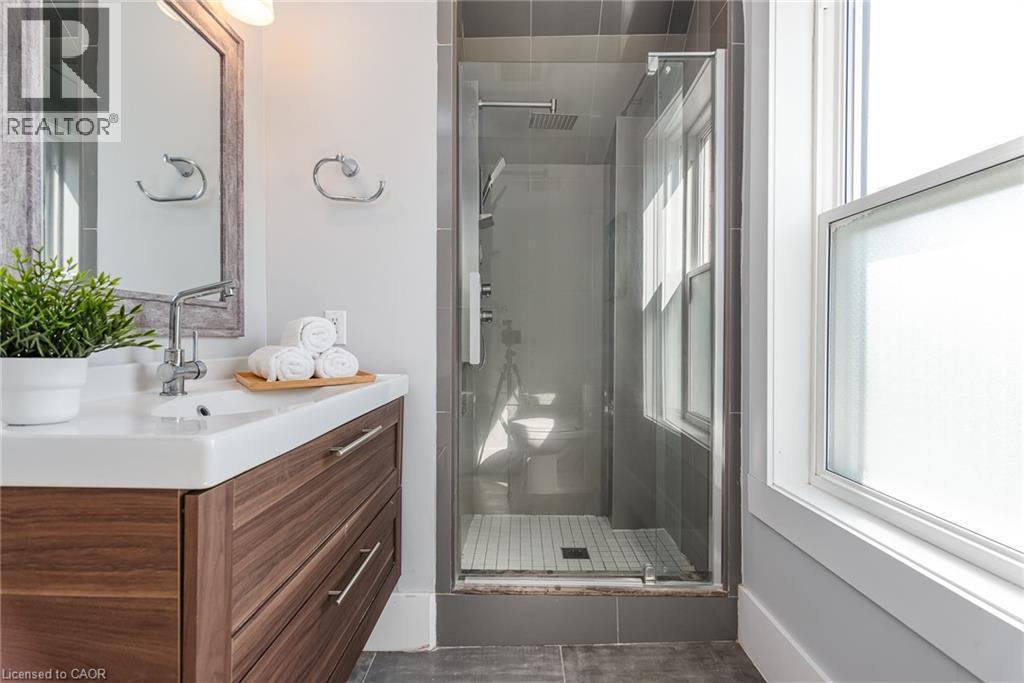 Contemporary bathroom featuring a wood-finish vanity with an integrated sink, polished chrome faucet, and a large mirrored cabinet - 40 Woodland Avenue, Kitchener, ON