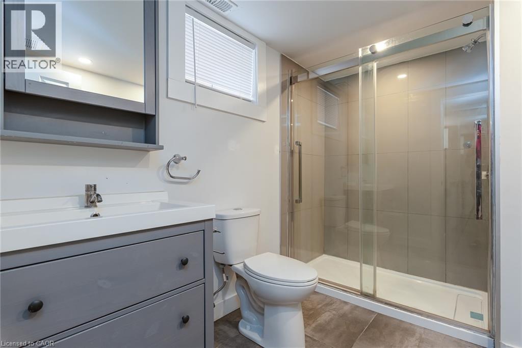 Contemporary bathroom featuring a spacious glass-enclosed shower with tiled walls and a white base, a gray vanity with an integrated white sink, a chrome faucet, and a wall-mounted medicine cabinet wi - 40 Woodland Avenue, Kitchener, ON