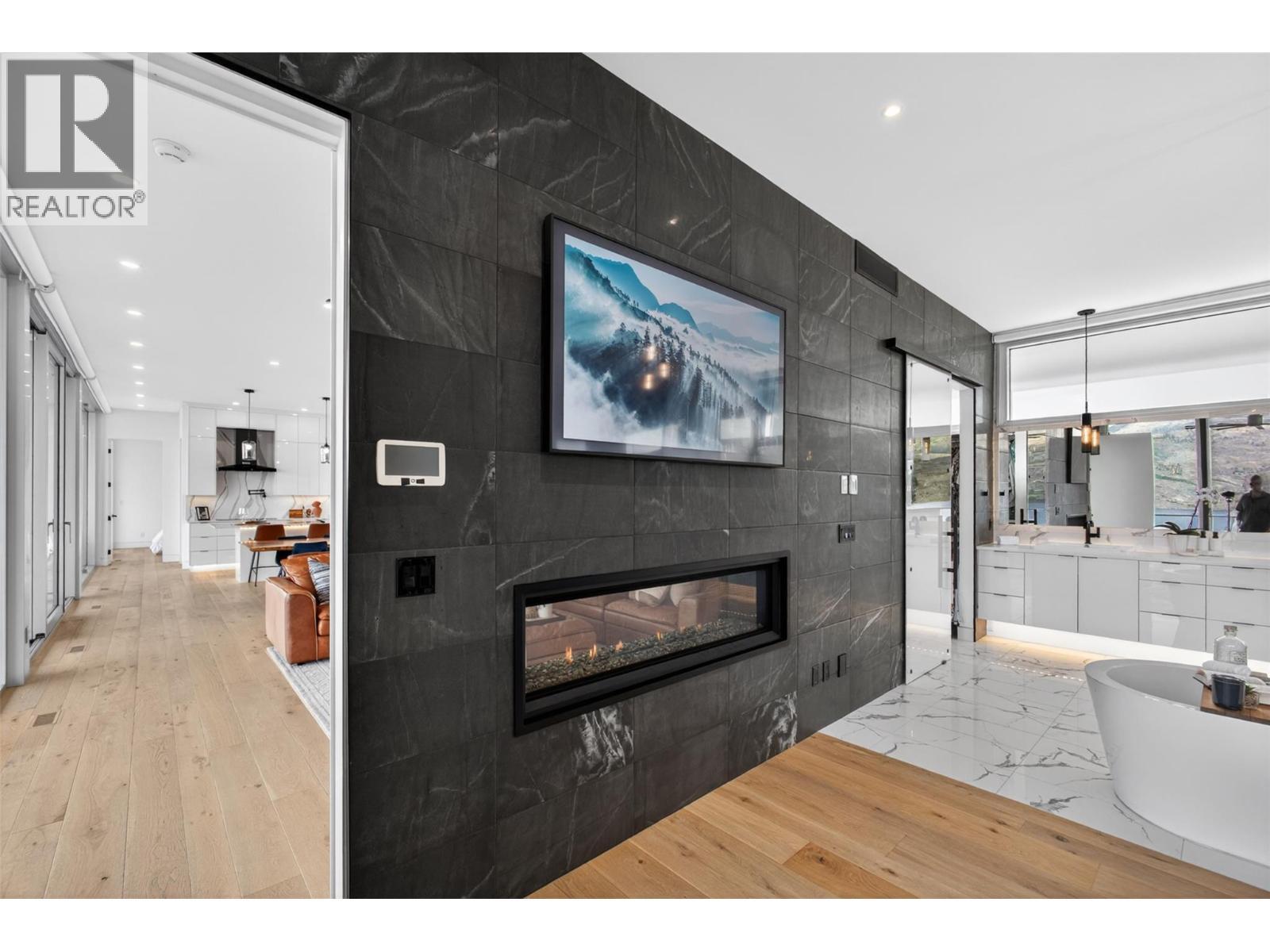 A dramatic real stone feature wall supplied by K2 Stone in Kelowna serves as a major architectural focal point within the suite as you enjoy the two-sided 5.5' linear fireplace. - 5835 Vicary Road, Peachland, BC