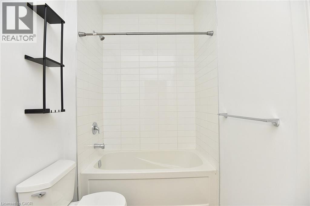 Bathroom featuring a built-in tub with white subway tile surround, chrome fixtures, and a wall-mounted shelving unit - 4040 Upper Middle Road Unit# 105, Burlington, ON