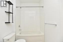 Bathroom featuring a built-in tub with white subway tile surround, chrome fixtures, and a wall-mounted shelving unit -