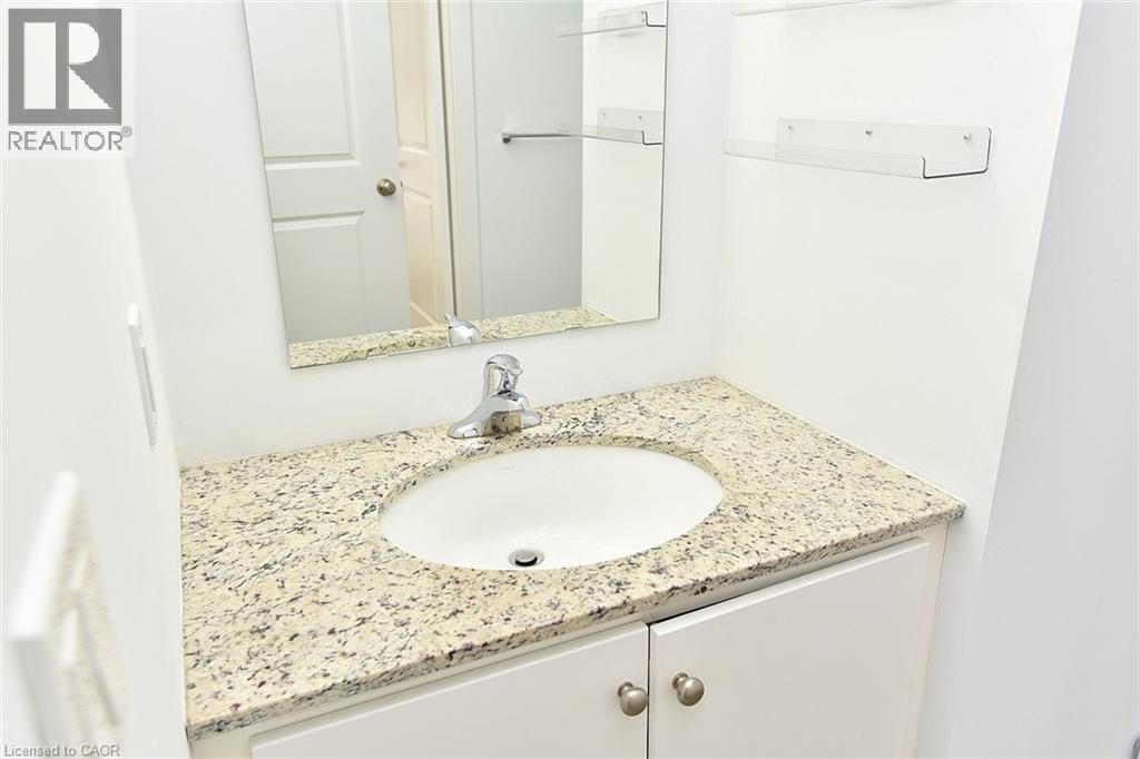 Vanity featuring a white oval sink, granite countertop, chrome faucet, white cabinetry, and brushed nickel hardware - 4040 Upper Middle Road Unit# 105, Burlington, ON