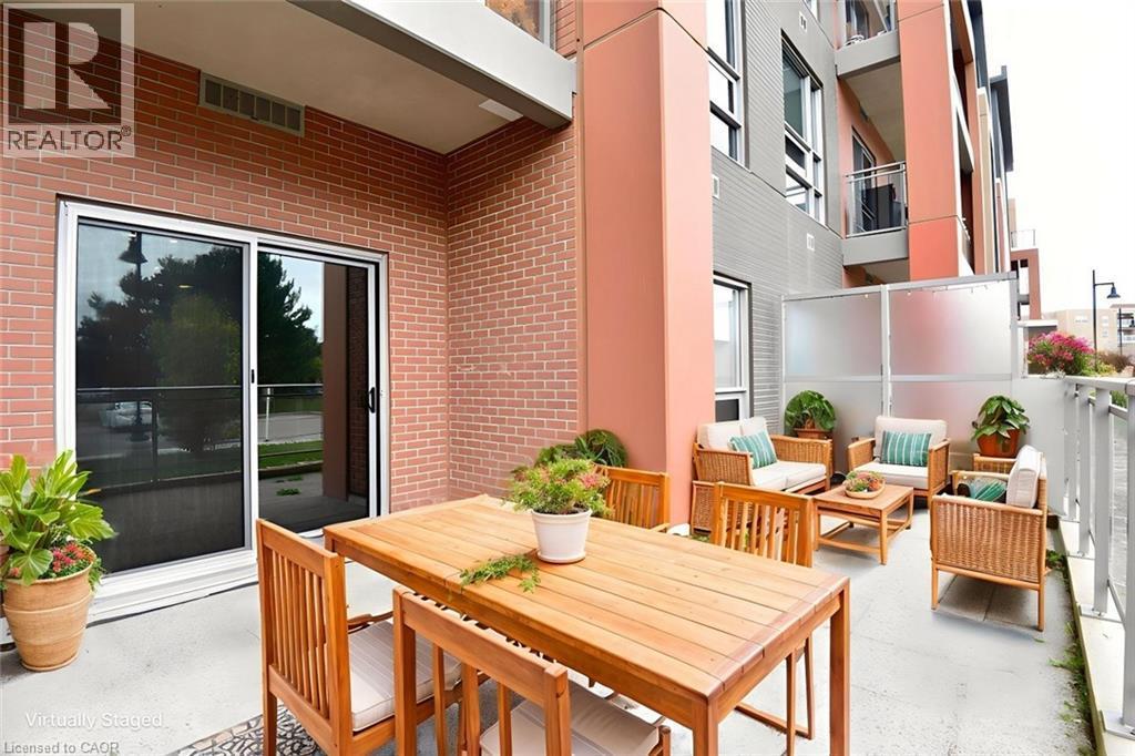 Private patio featuring brick cladding, sliding glass doors, concrete flooring, and a frosted glass privacy screen - 4040 Upper Middle Road Unit# 105, Burlington, ON
