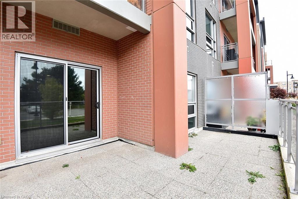 Ground-level patio featuring a sliding glass door entry, brick exterior, and a frosted privacy screen - 4040 Upper Middle Road Unit# 105, Burlington, ON