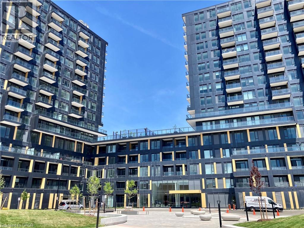 Modern high-rise residential building featuring a dark facade with geometric yellow accents - 4878 Powers Common Unit# C-1105, Burlington, ON