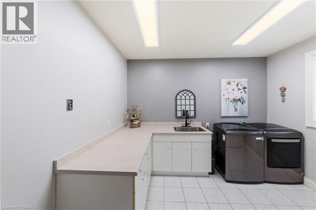 Laundry room featuring a built-in utility sink with a black faucet, white cabinetry, extensive countertop space, washer and dryer and tile flooring - 7775 St. Augustine Crescent, Niagara Falls, ON