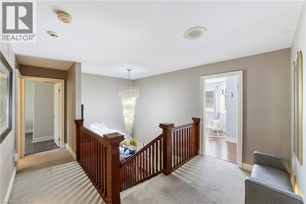 Upper-level hallway featuring a striking multi-tiered chandelier, rich wood stair railing, soft light-toned carpet flooring, and neutral wall tones - 7775 St. Augustine Crescent, Niagara Falls, ON