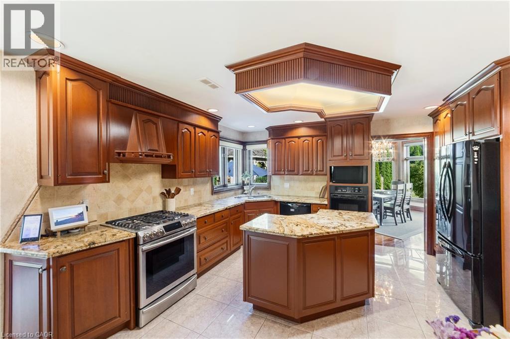Kitchen featuring rich wood cabinetry, patterned tile flooring, granite countertops, stainless steel appliances, 2 ovens, walk-in pantry not shown - 7775 St. Augustine Crescent, Niagara Falls, ON