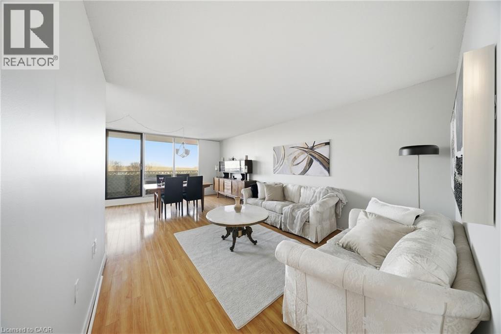 Open-concept living area featuring wood-finish flooring, white walls, and a dedicated dining space - 2055 Upper Middle Road Unit# 602, Burlington, ON