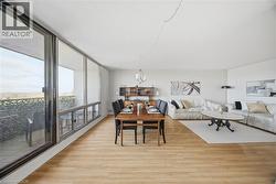 Open-concept living space with expansive wall-to-wall windows, light wood-finish flooring, and a dedicated dining area -