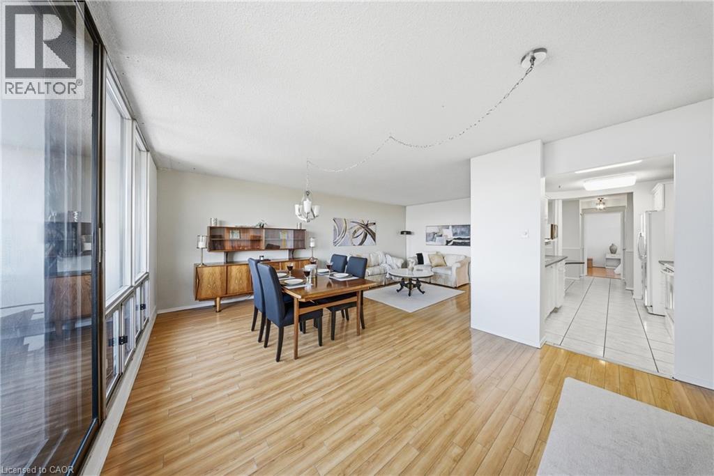 Open-concept living space featuring wood-finish flooring, a wall of windows, and a dedicated dining area with an overhead chandelier - 2055 Upper Middle Road Unit# 602, Burlington, ON