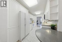Bright kitchen featuring extensive white cabinetry, white appliances, tiled flooring, and a curved countertop with integrated sink -