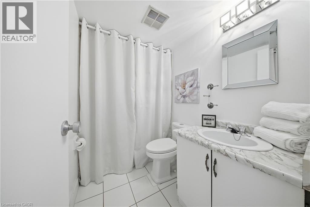White tiled bathroom featuring a vanity with a white countertop, an undermount sink, and a framed mirror - 2055 Upper Middle Road Unit# 602, Burlington, ON