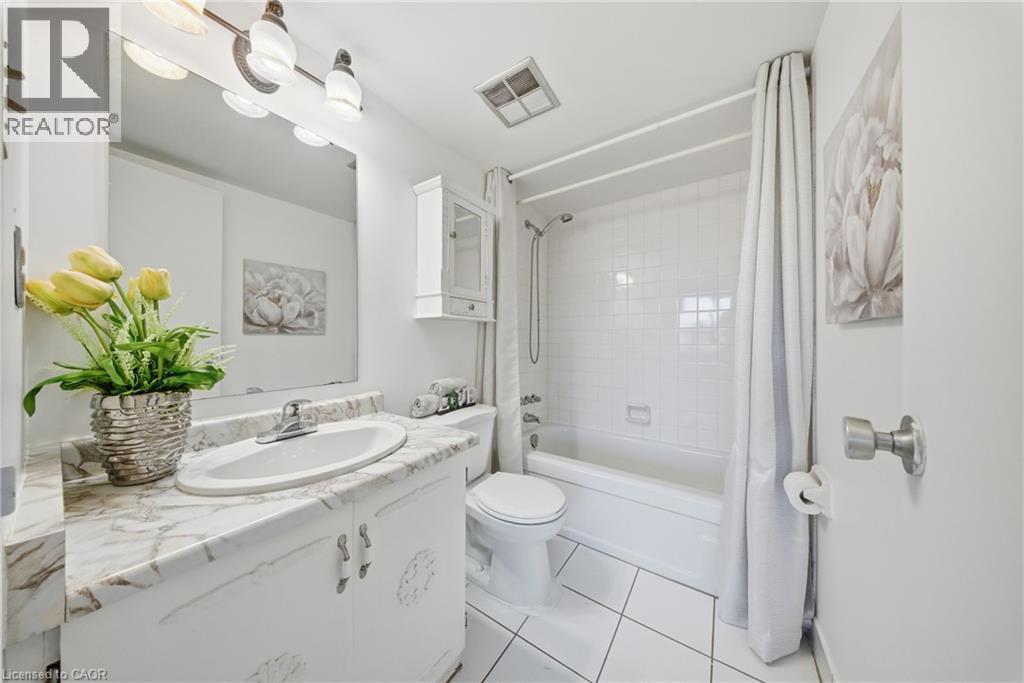 Bathroom featuring a white vanity with a marble-finish countertop, an oval undermount sink, and a three-bulb vanity light fixture - 2055 Upper Middle Road Unit# 602, Burlington, ON