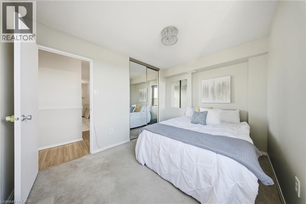 Carpeted sleeping area featuring a mirrored closet, a crystal chandelier, and a recessed wall niche - 2055 Upper Middle Road Unit# 602, Burlington, ON