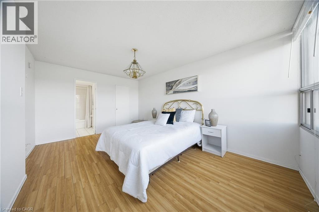 Bright room featuring wood-finish flooring, a contemporary ceiling light fixture, and a large window - 2055 Upper Middle Road Unit# 602, Burlington, ON