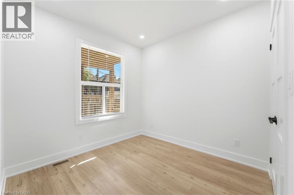 Room featuring light wood-finish flooring, white painted walls, and a single window with horizontal blinds - 968 Main Street E, Hamilton, ON