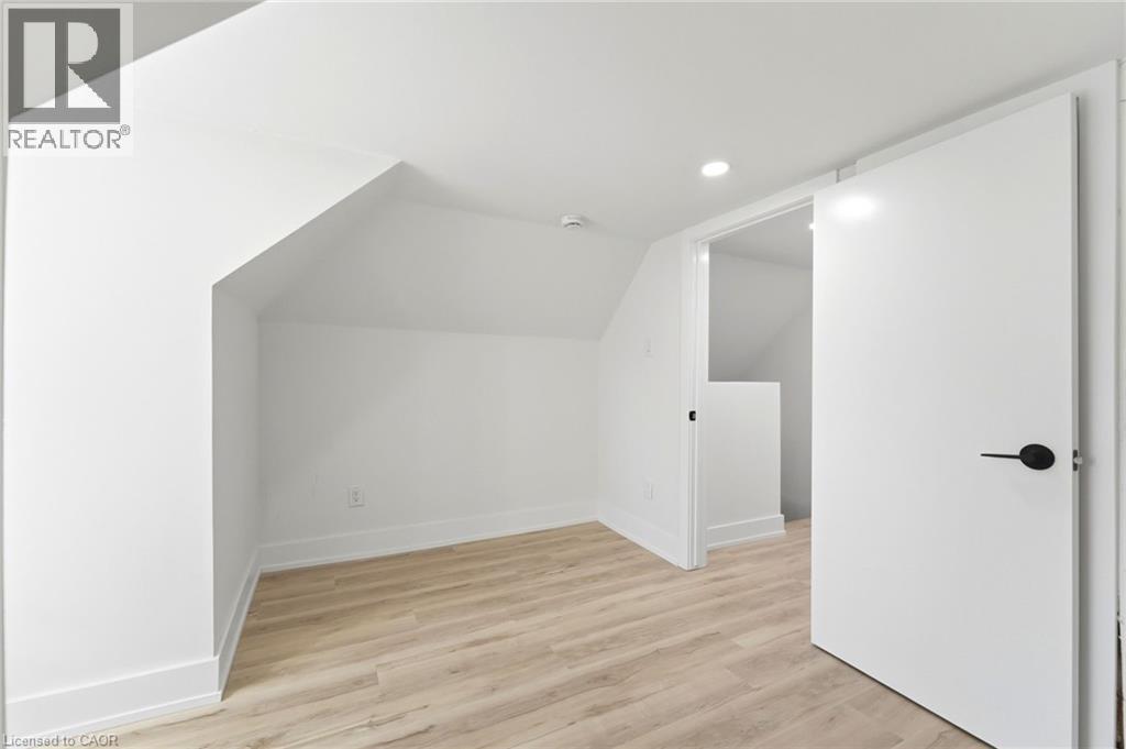 Finished attic space featuring light wood-finish flooring, crisp white walls, recessed lighting, and a modern slab door with matte black hardware - 968 Main Street E, Hamilton, ON - Indoor Photo Showing Other Room