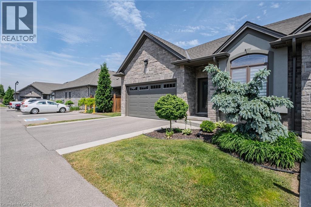 Stone and stucco exterior featuring an attached garage, arched window, and mature landscaping - 15 Winterberry Lane, Waterford, ON