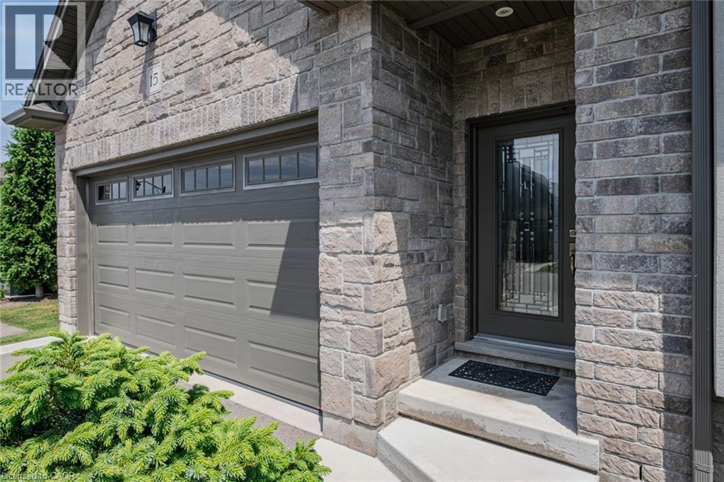 Stone facade with integrated garage featuring upper window panels, concrete steps, and a decorative glass entry door - 15 Winterberry Lane, Waterford, ON