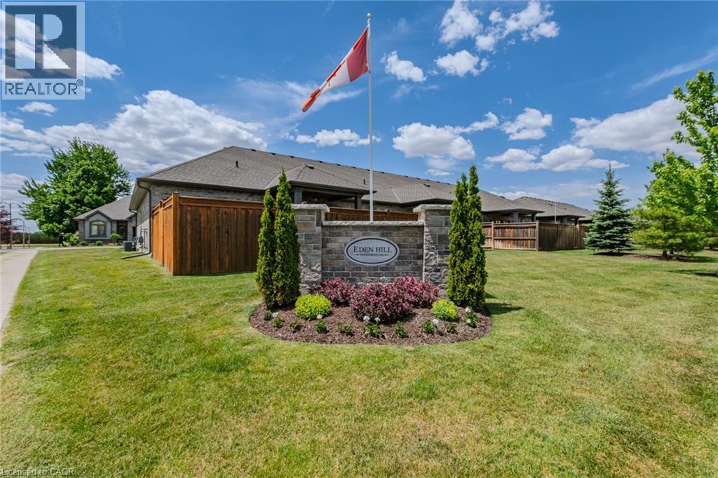 Stone monument with a Canadian flag, surrounded by landscaped plantings and mature trees - 15 Winterberry Lane, Waterford, ON