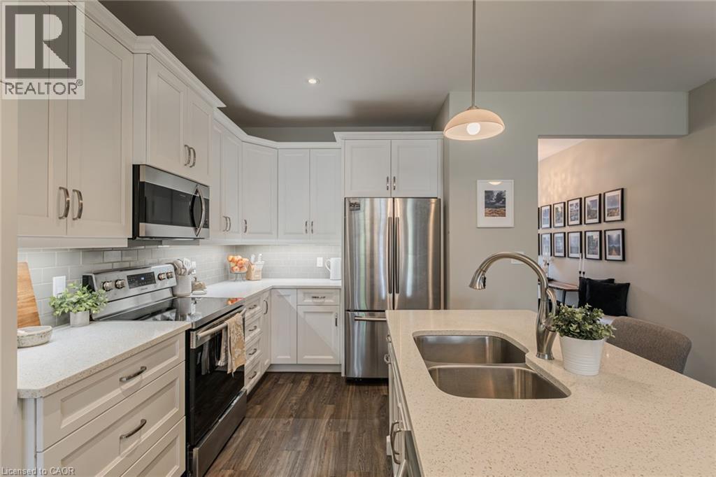 Contemporary kitchen featuring white cabinetry, stainless steel appliances, a double basin sink, light-toned countertops, and wood-finish flooring - 15 Winterberry Lane, Waterford, ON