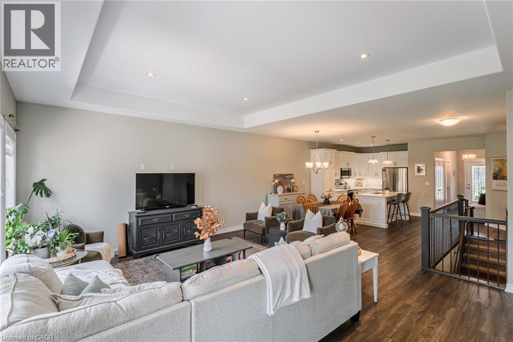 Open-concept living area featuring tray ceilings with recessed lighting, wood-finish flooring, and a kitchen with white cabinetry and stainless steel appliances - 15 Winterberry Lane, Waterford, ON