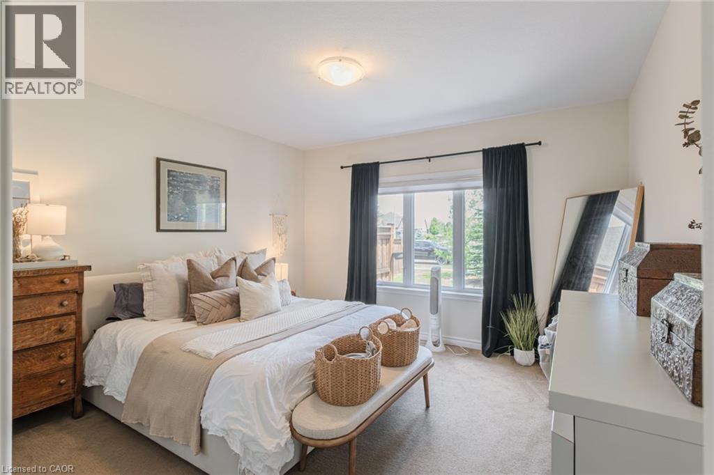 Carpeted bedroom featuring a large window with dark drapery panels, a flush-mount ceiling light fixture, and light-toned wall paint - 15 Winterberry Lane, Waterford, ON
