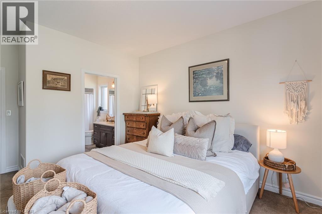 Spacious bedroom featuring light-toned walls, neutral carpeting, and a doorway to a bathroom with a dark wood-finish vanity and white countertop - 15 Winterberry Lane, Waterford, ON