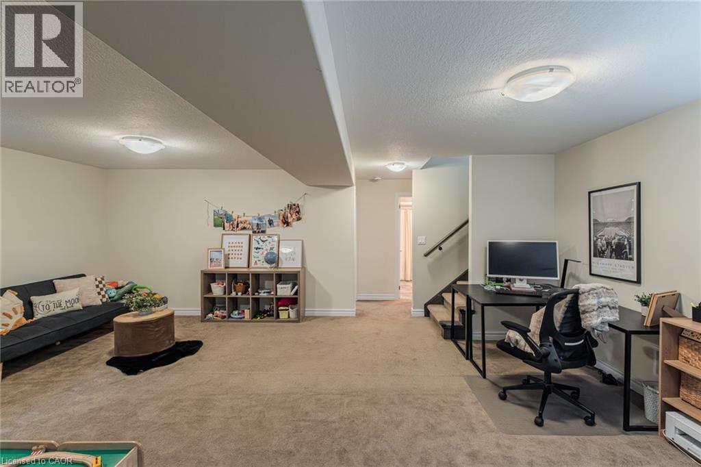 Expansive carpeted room featuring a built-in staircase with dark wood handrail, light beige walls, and flush-mount ceiling lighting - 15 Winterberry Lane, Waterford, ON
