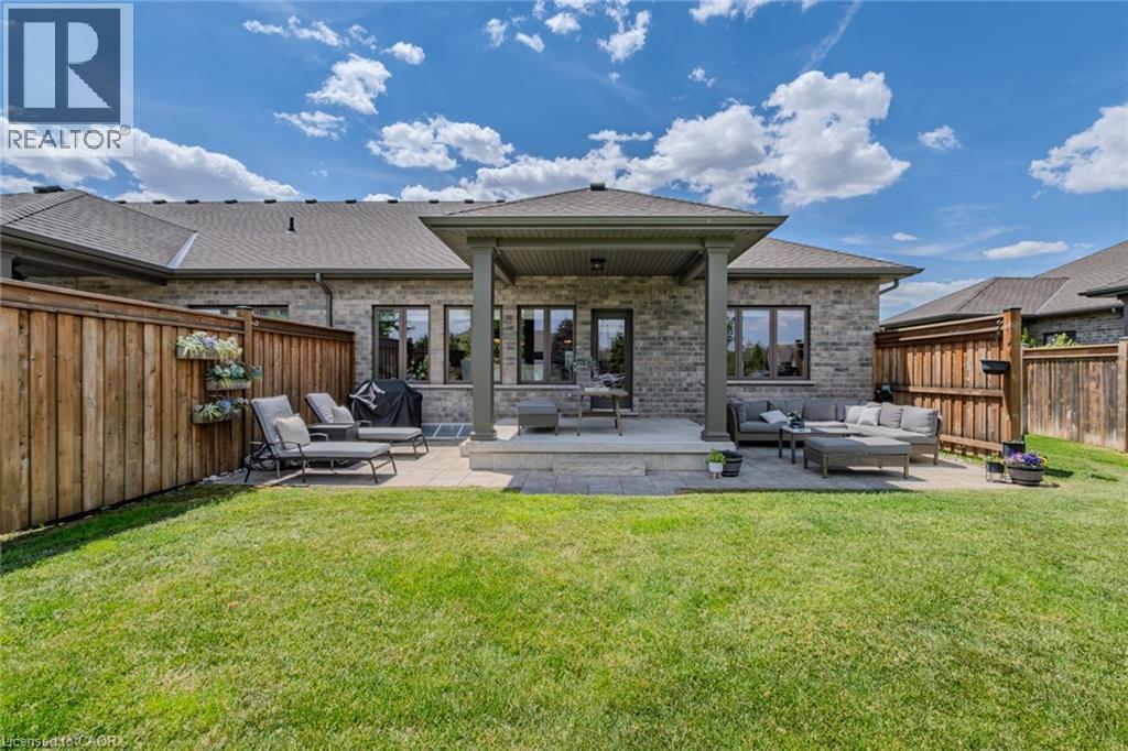 Expansive backyard featuring a stone paver patio, covered porch area, full privacy fencing, and brick exterior - 15 Winterberry Lane, Waterford, ON