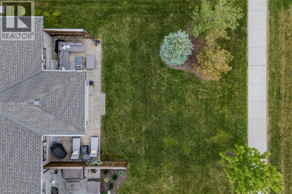 Expansive green lawn with mature landscaping, a concrete sidewalk, and two distinct patio areas featuring paver stones - 15 Winterberry Lane, Waterford, ON